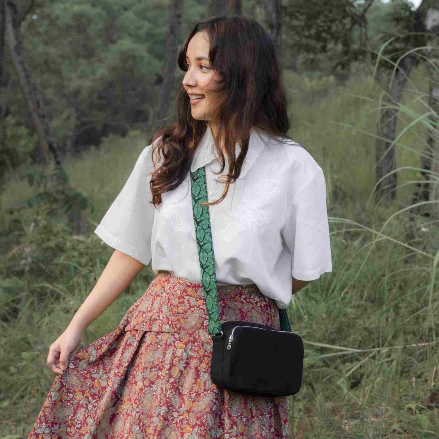 A girl with a box sling bag. She is wearing a white shirt with printed skirt and carrying black leaves box sling bag